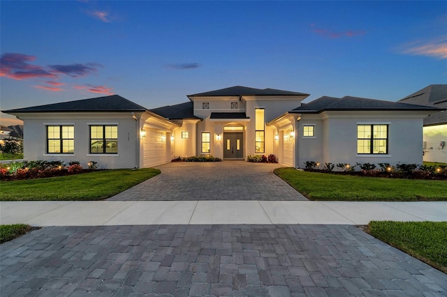 prairie-style home featuring stucco siding, an attached garage, decorative driveway, and a front yard