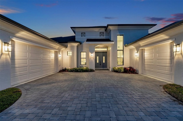 view of front facade featuring stucco siding, french doors, decorative driveway, and a garage