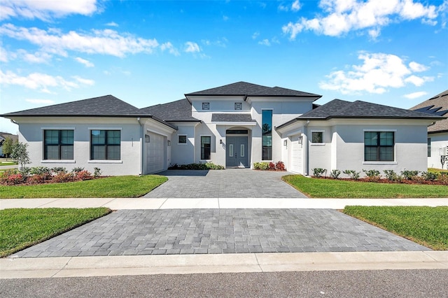 prairie-style house with decorative driveway, a front lawn, an attached garage, and stucco siding