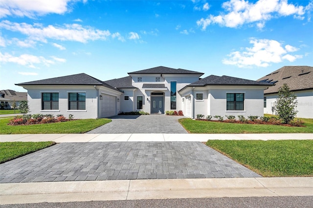 prairie-style house featuring stucco siding, an attached garage, decorative driveway, and a front yard