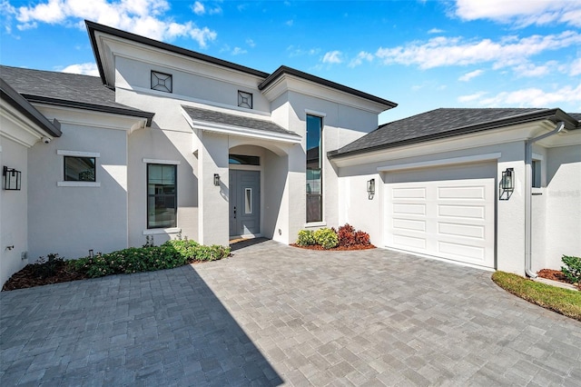 view of front of house featuring a shingled roof, decorative driveway, a garage, and stucco siding