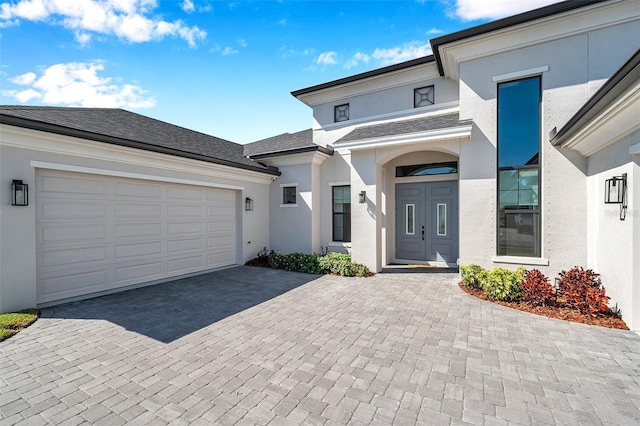 view of front of property with decorative driveway, roof with shingles, an attached garage, and stucco siding