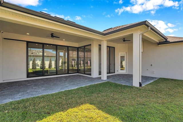 rear view of property featuring a yard, ceiling fan, stucco siding, and a patio area