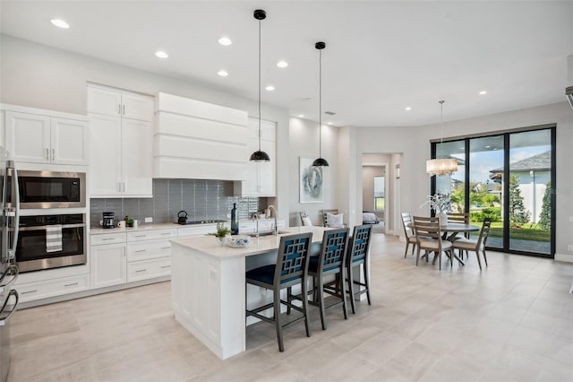 kitchen featuring tasteful backsplash, built in microwave, a center island with sink, light countertops, and stainless steel oven