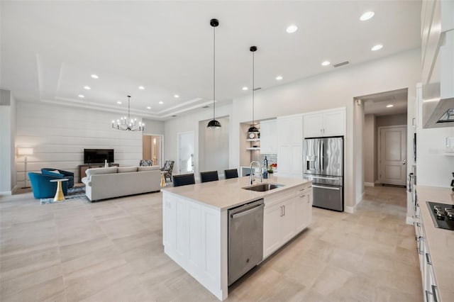 kitchen featuring a tray ceiling, a kitchen island with sink, a sink, stainless steel appliances, and white cabinets