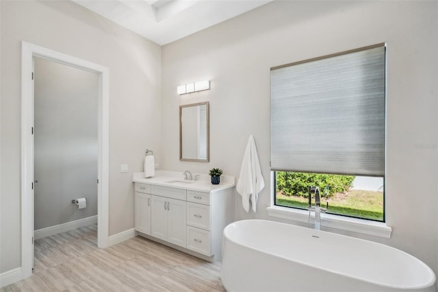 full bathroom with wood finished floors, vanity, baseboards, and a freestanding tub