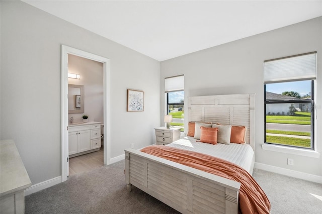 bedroom featuring light carpet, ensuite bathroom, and baseboards