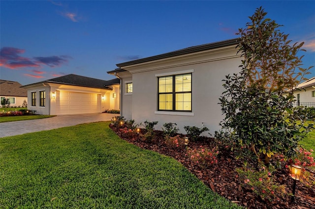 view of front of home with stucco siding, driveway, a lawn, and a garage