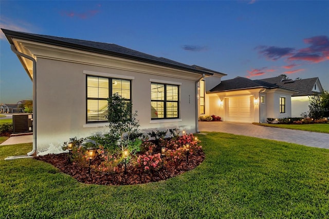 view of front of property featuring central air condition unit, stucco siding, a yard, a garage, and driveway