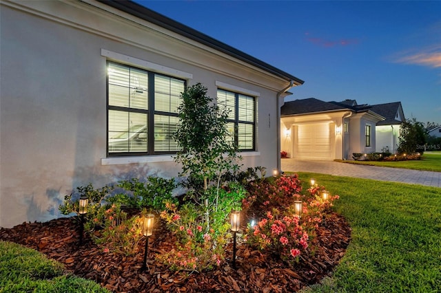 view of side of property featuring stucco siding, an attached garage, driveway, and a lawn