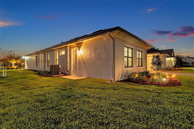 view of side of home featuring a lawn, central AC, and stucco siding