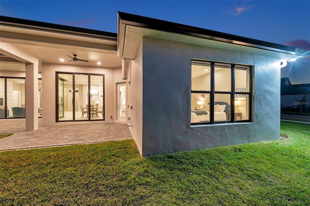 back of house with stucco siding, a lawn, and a patio area