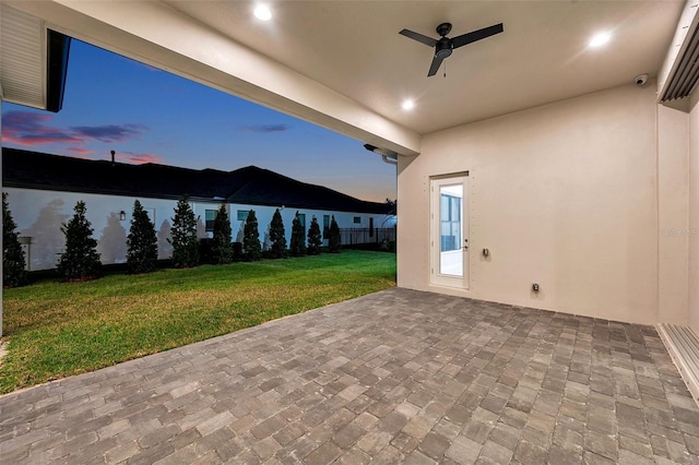 patio terrace at dusk featuring ceiling fan and a yard