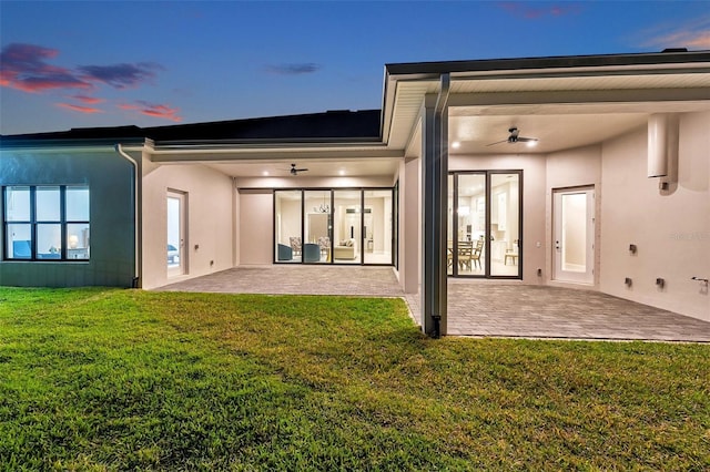 rear view of property with a ceiling fan, a patio, a lawn, and stucco siding