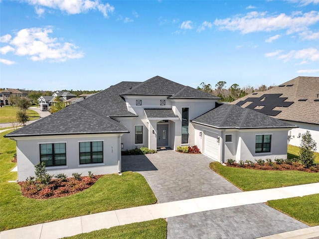 view of front facade with a front yard, an attached garage, stucco siding, a shingled roof, and decorative driveway