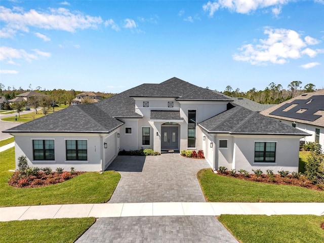 view of front of house with decorative driveway, a shingled roof, a front yard, and stucco siding