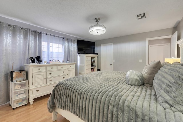 bedroom with visible vents, a textured ceiling, and light wood-style floors