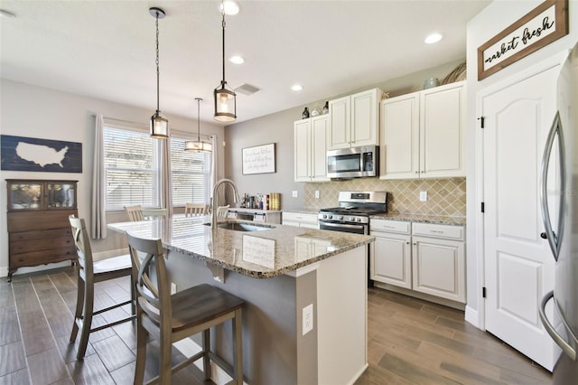 kitchen featuring visible vents, a sink, appliances with stainless steel finishes, a kitchen breakfast bar, and backsplash