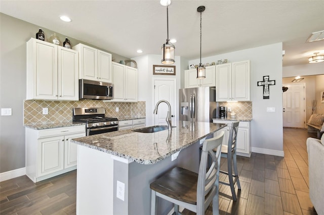 kitchen featuring light stone countertops, wood tiled floor, a breakfast bar area, stainless steel appliances, and a sink