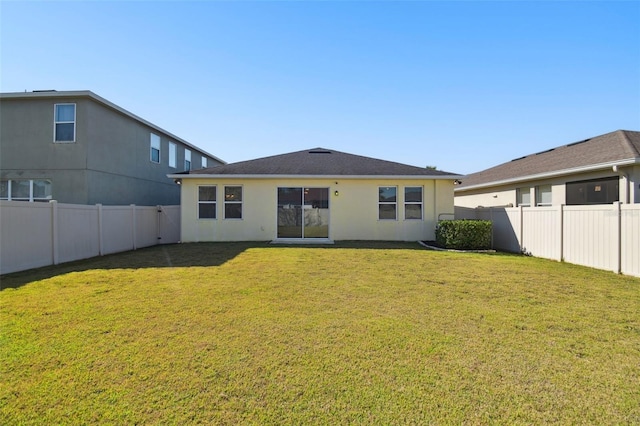 back of house with stucco siding, a lawn, and a fenced backyard