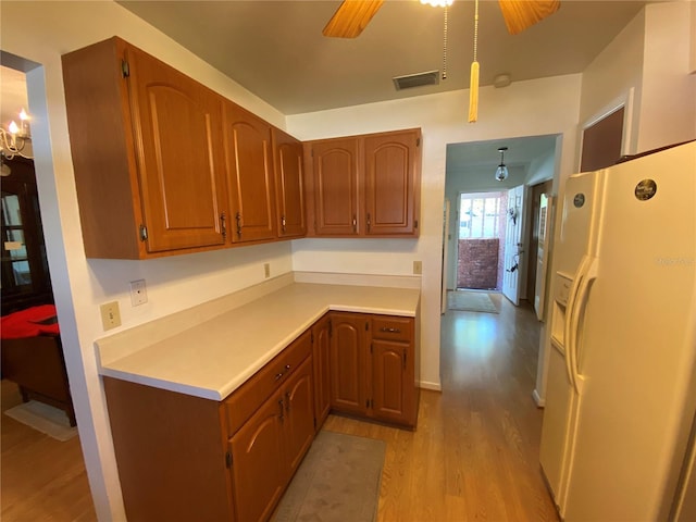 kitchen featuring visible vents, a ceiling fan, white fridge with ice dispenser, light wood finished floors, and light countertops