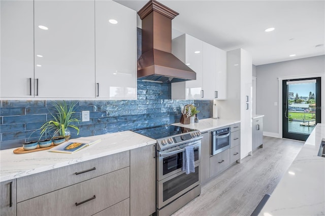 kitchen featuring modern cabinets, stainless steel appliances, light wood-style floors, wall chimney range hood, and light stone countertops