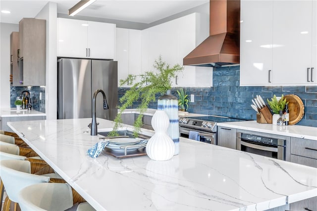 kitchen featuring light stone counters, appliances with stainless steel finishes, modern cabinets, and wall chimney exhaust hood