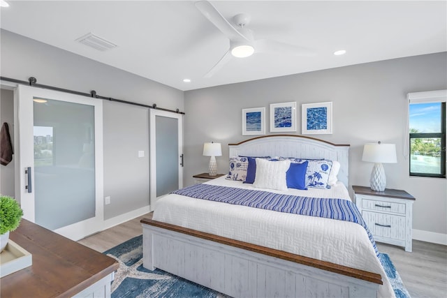 bedroom with visible vents, baseboards, light wood-style floors, and a barn door