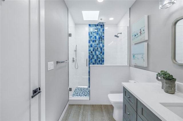 bathroom featuring toilet, a stall shower, wood finished floors, a skylight, and vanity