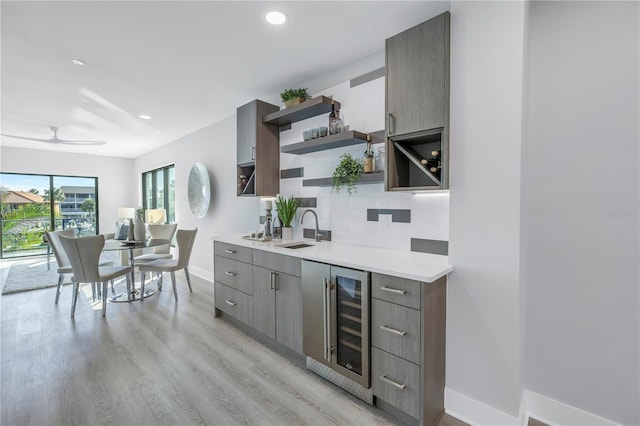 kitchen with beverage cooler, light wood-type flooring, open shelves, light countertops, and tasteful backsplash