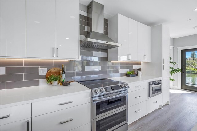 kitchen featuring decorative backsplash, light countertops, wall chimney range hood, and appliances with stainless steel finishes