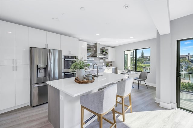 kitchen featuring modern cabinets, backsplash, stainless steel appliances, wall chimney exhaust hood, and light countertops