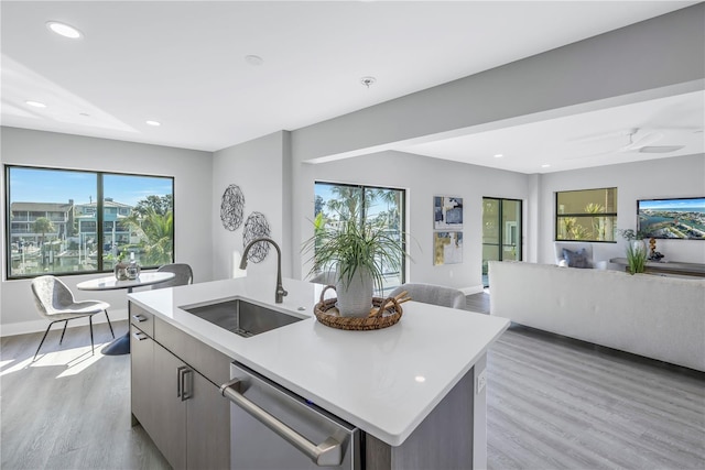 kitchen with an island with sink, a sink, light countertops, stainless steel dishwasher, and open floor plan