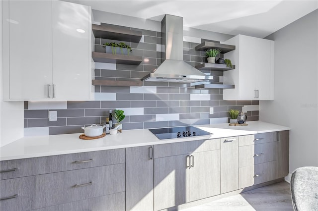 kitchen featuring open shelves, light countertops, black electric stovetop, wall chimney exhaust hood, and backsplash