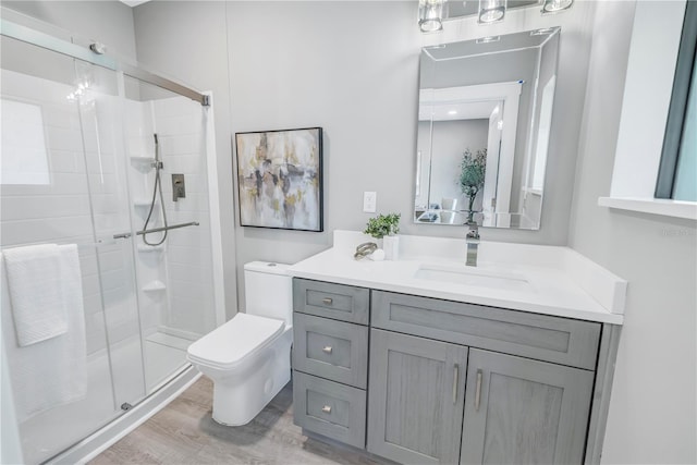 bathroom featuring vanity, toilet, wood finished floors, and a stall shower