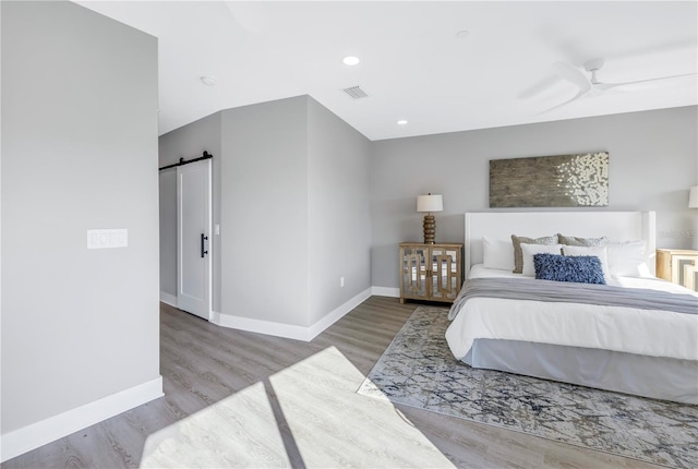 bedroom featuring visible vents, a barn door, baseboards, and wood finished floors