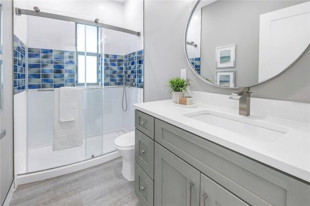 bathroom featuring wood finished floors, toilet, a stall shower, and vanity