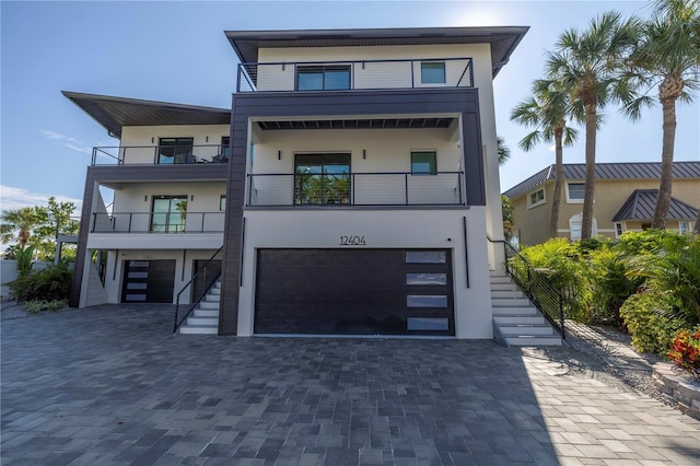 contemporary house with stairway, a garage, driveway, and stucco siding