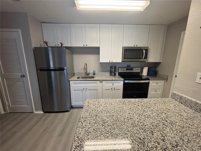 kitchen with a sink, light stone counters, appliances with stainless steel finishes, and white cabinets