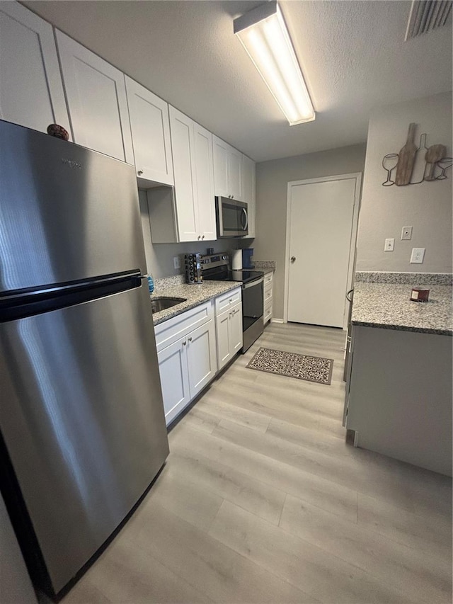 kitchen featuring visible vents, light wood finished floors, white cabinets, appliances with stainless steel finishes, and a textured ceiling