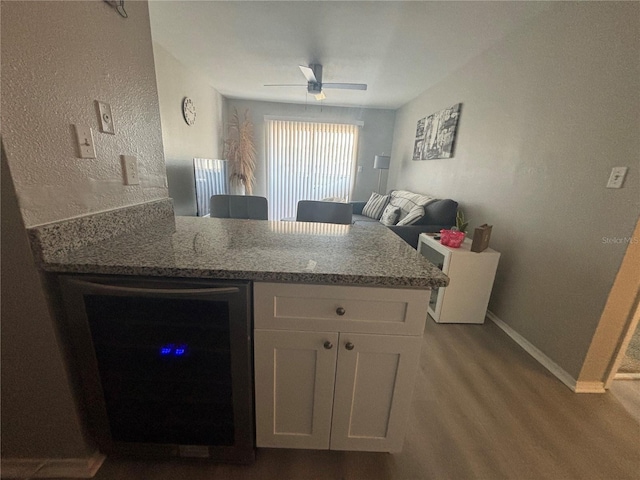 kitchen with a ceiling fan, white cabinetry, wine cooler, a peninsula, and stone counters