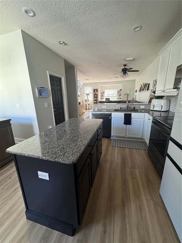 kitchen with a peninsula, wood finished floors, white cabinets, black appliances, and a ceiling fan