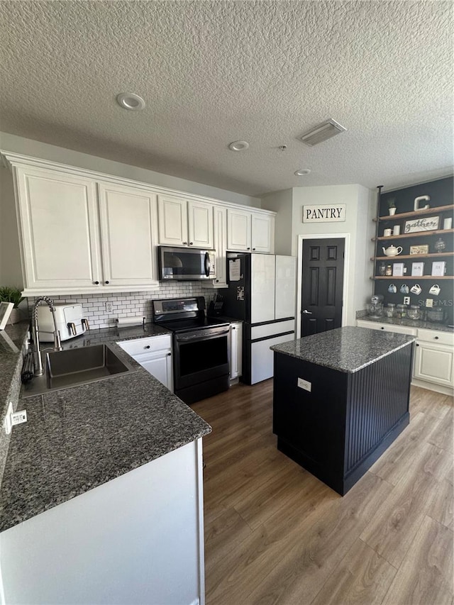 kitchen with a kitchen island, light wood-style flooring, white cabinets, stainless steel appliances, and a sink