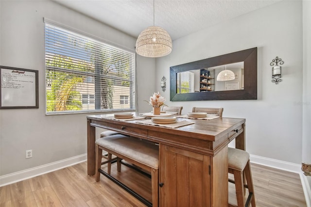 dining room with light wood-type flooring, baseboards, and a textured ceiling