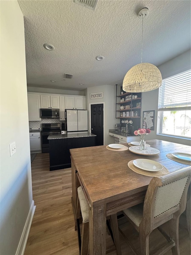 dining room featuring visible vents, a textured ceiling, baseboards, and wood finished floors