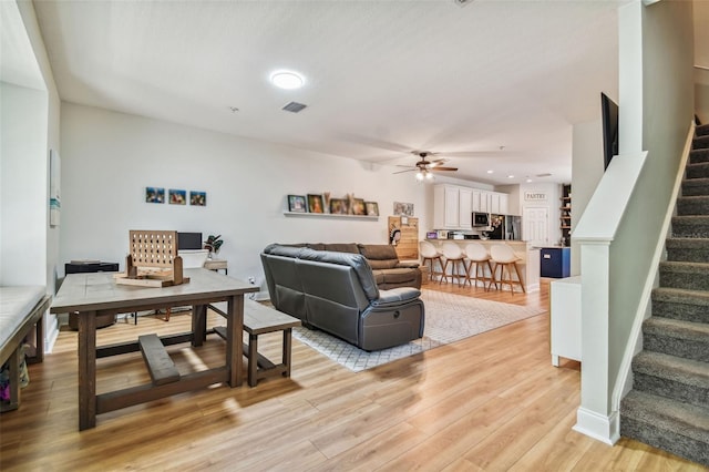 living room featuring light wood-type flooring, visible vents, recessed lighting, ceiling fan, and stairs