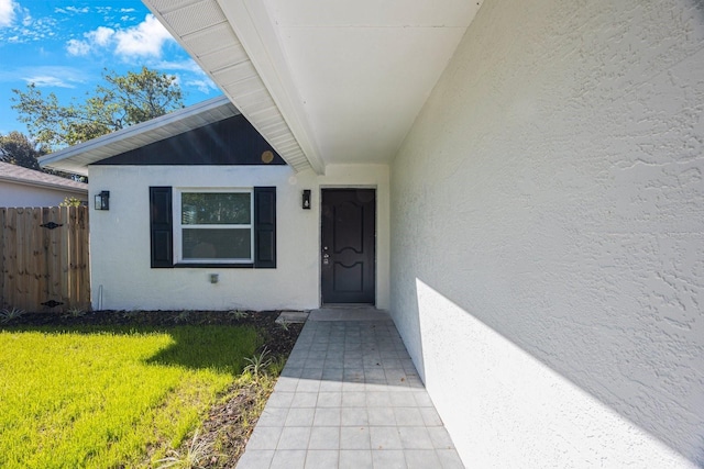 doorway to property with stucco siding, a yard, and fence