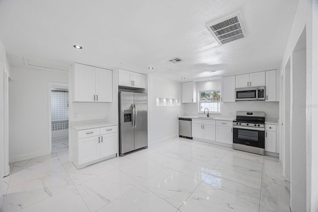 kitchen featuring visible vents, a sink, stainless steel appliances, light countertops, and white cabinets