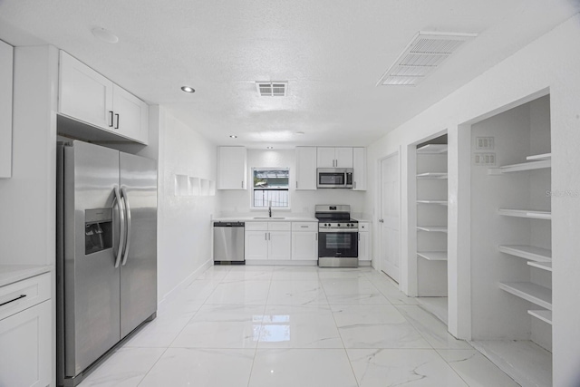 kitchen with visible vents, white cabinetry, stainless steel appliances, and a sink