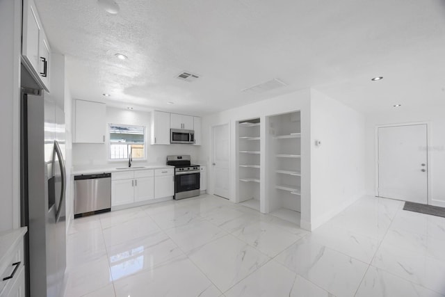 kitchen with light countertops, appliances with stainless steel finishes, white cabinets, marble finish floor, and a sink